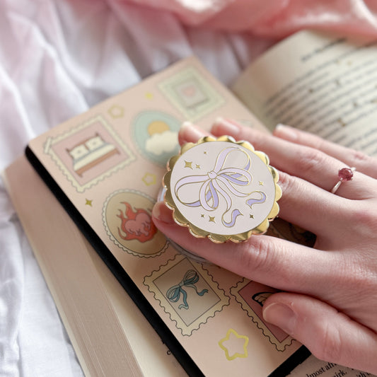 Hand holding a decorative paper clip over an open book with a pink fabric background