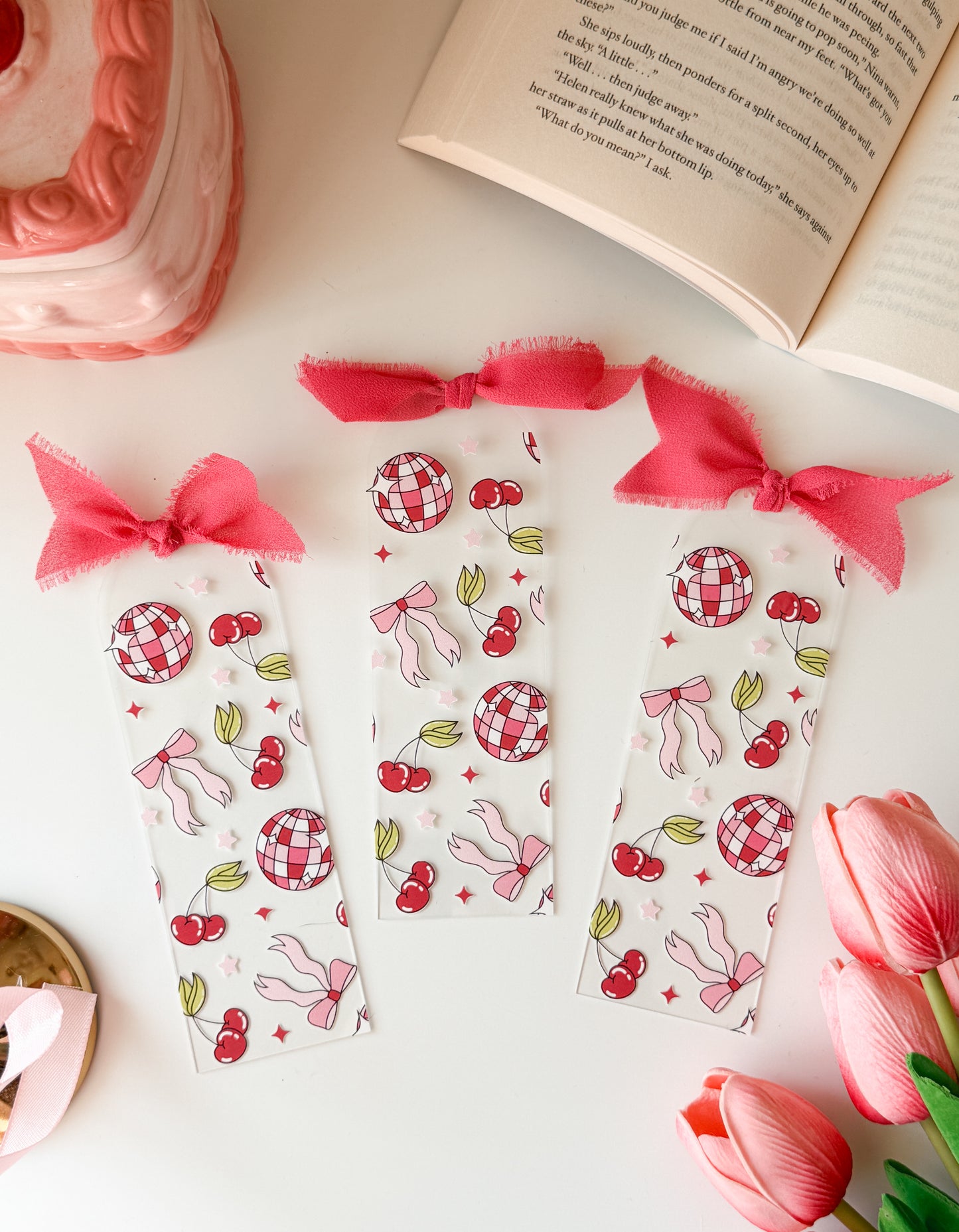 Set of decorative bookmarks with pink ribbons on a white surface with a book and tulips.