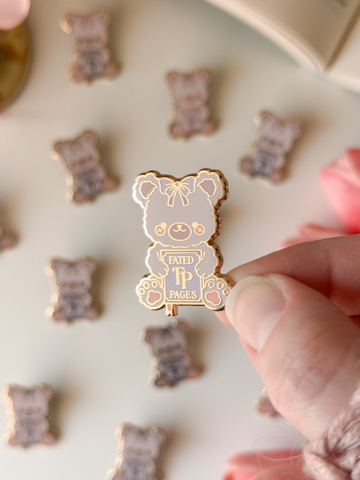 Gold bear-shaped pin with a purple label held by a hand against a background of similar pins.