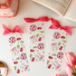 Set of decorative bookmarks with pink ribbons on a white surface with a book and tulips.