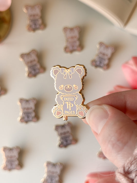 Gold bear-shaped pin with a purple label held by a hand against a background of similar pins.