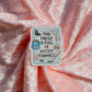 A rectangular enamel pin with rounded corners featuring hockey-themed illustrations and the text 'THIS KINDLE IS FULL OF HOCKEY ROMANCE' in black lettering, placed on draped pink satin fabric.