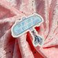 A die-cut sticker featuring a light blue sign that reads 'ON MY WAY TO THE BOY AROMAUM' with small white flowers and an illustration of ice skates, placed on pink glittery fabric.