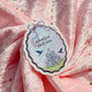 A die-cut sticker with a whimsical castle illustration and the text 'Adventure starts here' attached to a pink fabric backdrop with gold sequins.