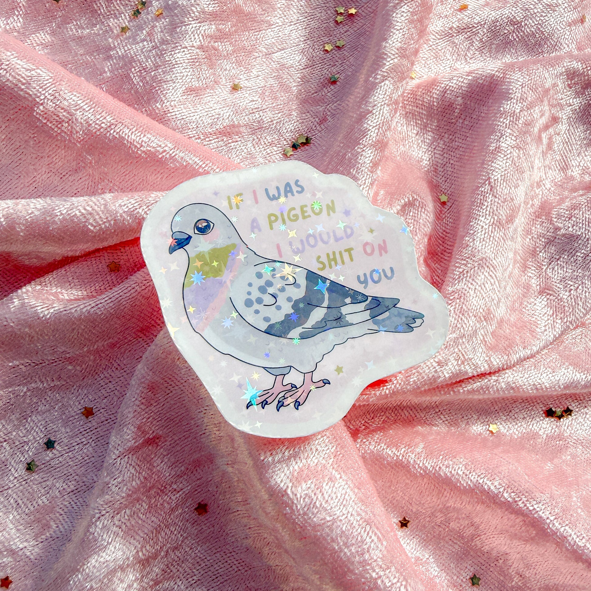 A die-cut sticker featuring a cartoon pigeon with the text 'IF I WAS A PIGEON I WOULD SHIT OR YOU' in pastel colors, placed on a shiny pink fabric background with scattered gold star confetti.